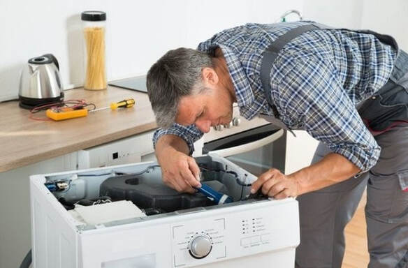 Appliance repairman in Plano fixing a whirlpool washer. The washing machine is pulled out of the counter and he is repairing the appliance with his tool.